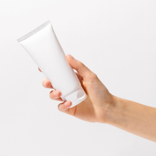 Mano sosteniendo un tubo blanco de crema