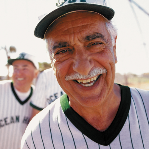 Hombre mayor sonriendo mientras usa un uniforme de béisbol y una gorra